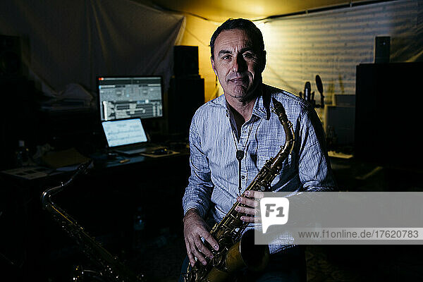 Smiling musician with saxophone sitting in recording studio