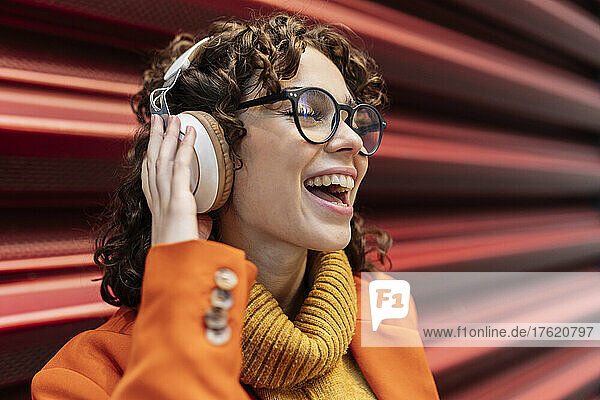 Happy woman listening music through headphones by wall