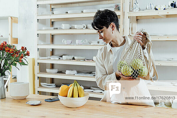 Entrepreneur holding mesh bag of fresh fruit by table