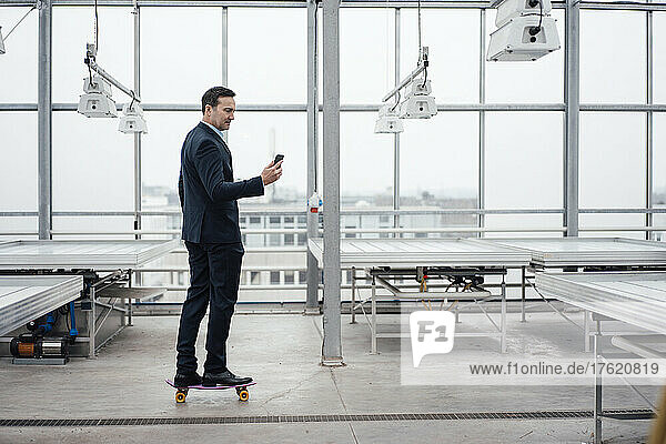 Businessman using mobile phone on skateboard in greenhouse