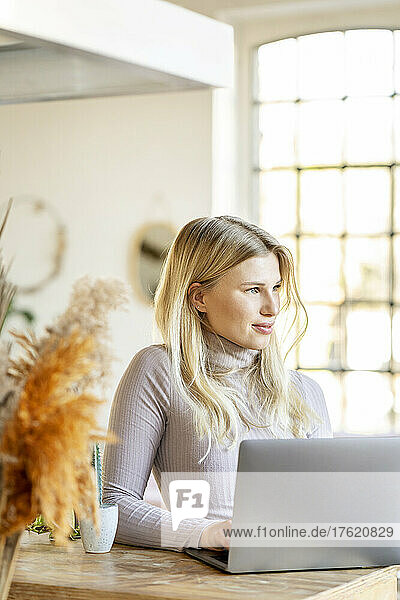 Schöne blonde Geschäftsfrau mit Laptop sitzt zu Hause