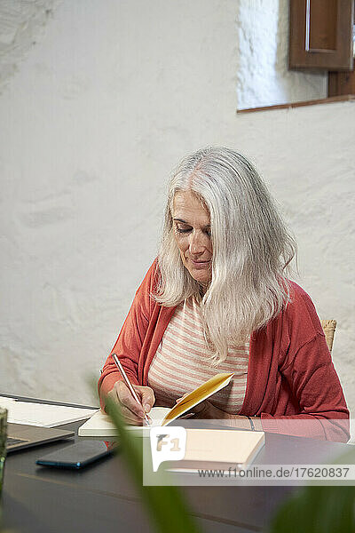 Freiberufler mit grauen Haaren schreibt zu Hause auf Notizblock