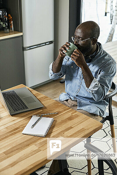 Businessman drinking tea looking at laptop on dining table at home