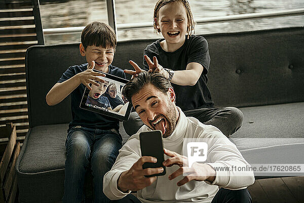 Playful man with sons taking selfie through smart phone at home
