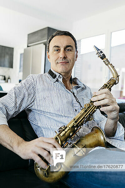 Smiling saxophonist with saxophone sitting on sofa at home