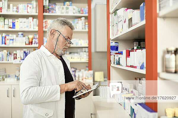 Pharmacist using tablet PC by shelf in pharmacy store