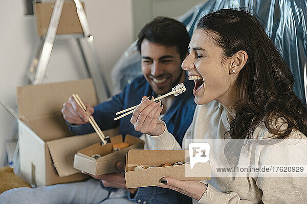 Young woman having sushi by boyfriend and relocating at new home