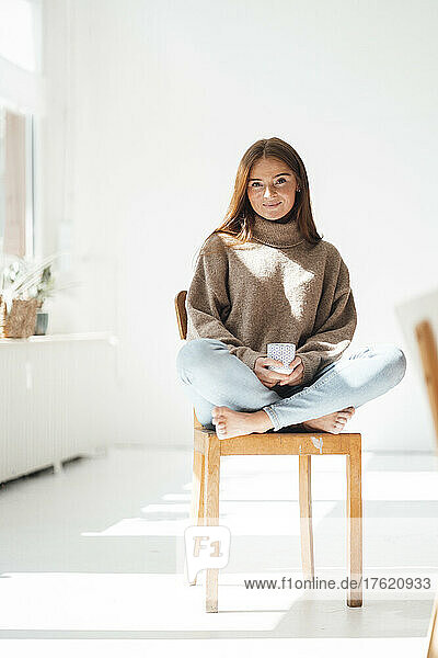 Young woman with coffee cup sitting on chair at home