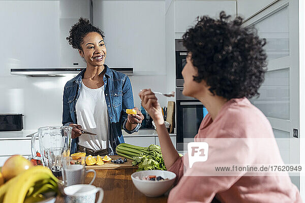 Woman giving slice of orange to friend in kitchen