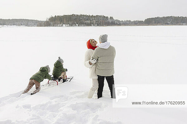 Couple embracing each other by sons tobogganing on snow in winter