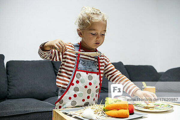Boy serving toy vegetables on plate at home