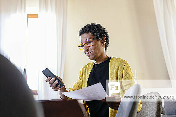 Businesswoman with paper document using smart phone at home