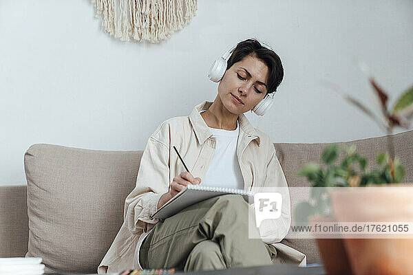 Artist with headphones sketching on notepad on sofa