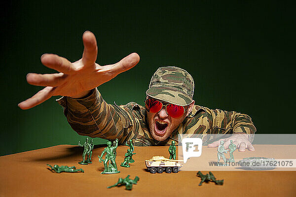 Military soldier in uniform screaming and reaching figurines on table