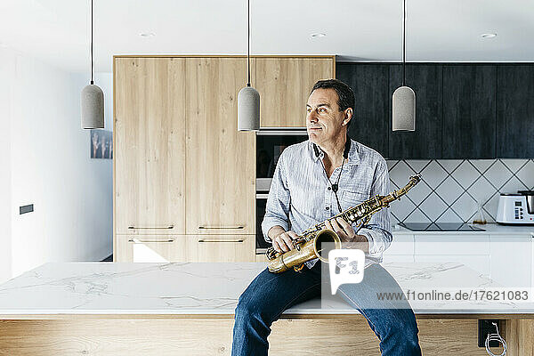 Saxophonist mit Saxophon sitzt zu Hause auf der Kücheninsel