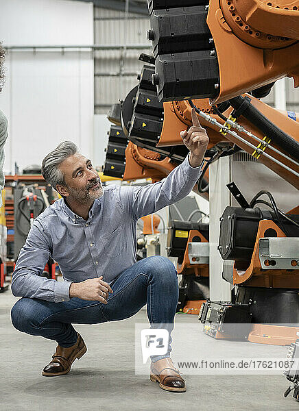 Engineer pointing at robotic arm examining in factory