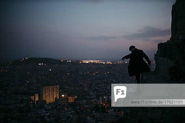 Man standing on rock in front of city at sunset