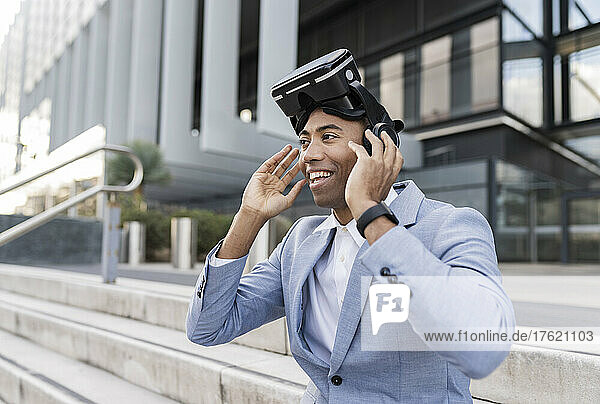 Smiling businessman wearing virtual reality simulator sitting in front of building
