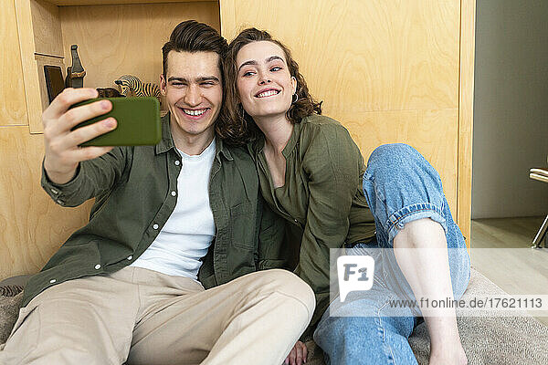 Happy young couple taking selfie through mobile phone at home