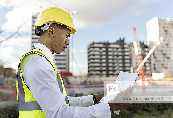 Engineer wearing hardhat reading blueprint at construction site