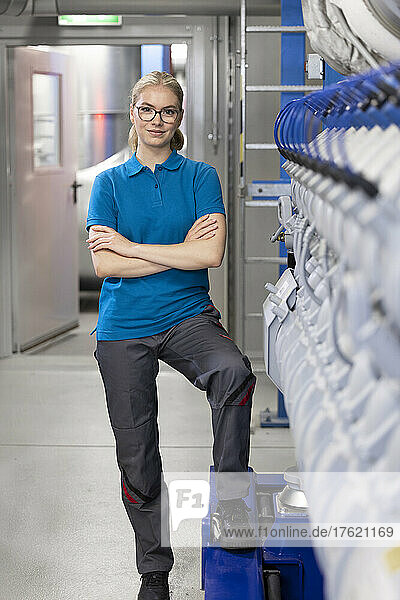 Smiling technician standing with arms crossed in factory