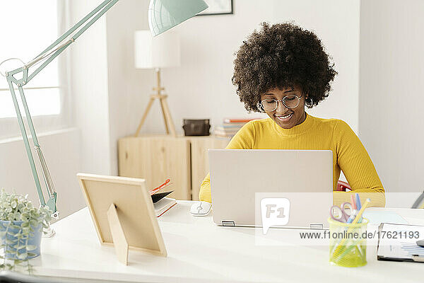Smiling freelancer using laptop sitting at table working from home