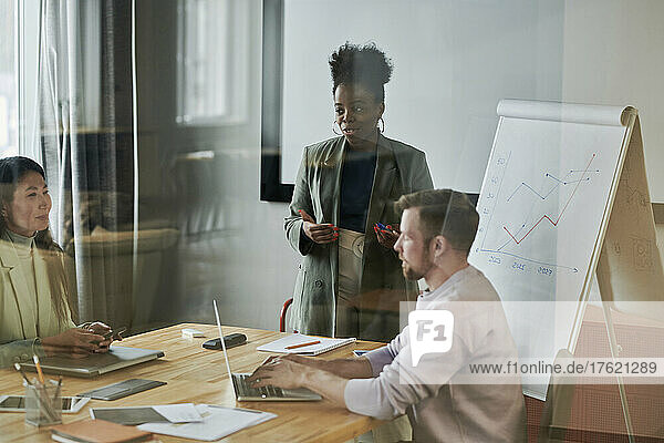 Business colleagues conducting meeting seen through glass wall in office