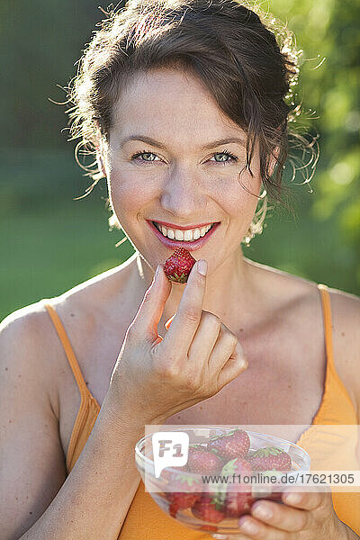 Smiling woman having strawberries on sunny day