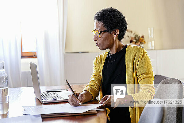 Businesswoman looking at laptop and doing paperwork in home office