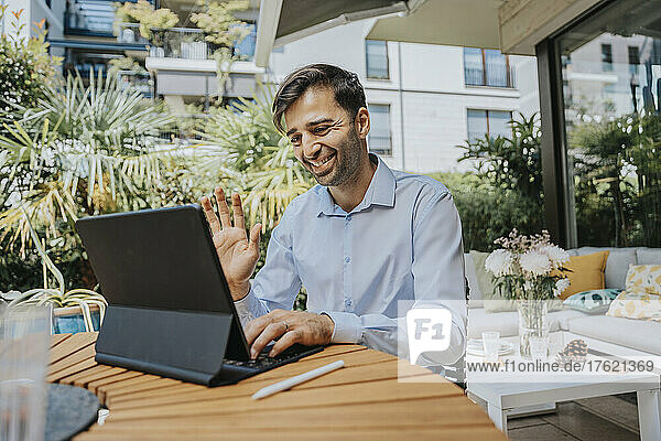 Smiling businessman waving on video call over tablet PC at back yard