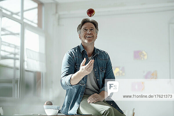 Smiling man throwing apple sitting on table