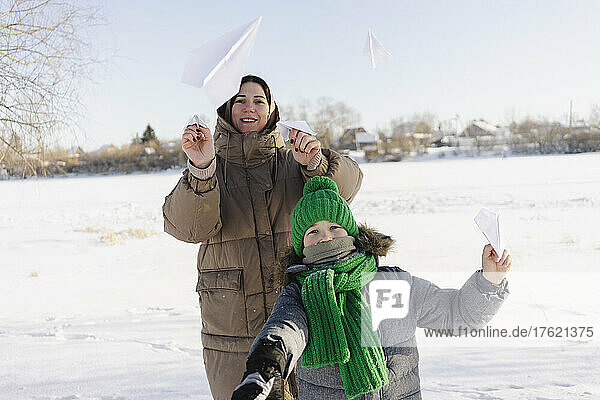 Happy mother and son playing with paper airplanes in snow