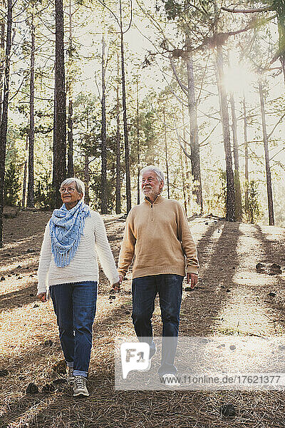 Happy senior couple in warm clothing walking together in forest