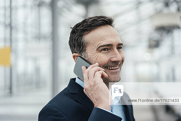 Happy businessman talking on mobile phone in greenhouse
