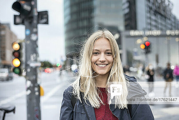 Lächelnde Frau mit blonden Haaren steht auf der Straße