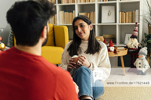 Woman holding cup sitting in front of boyfriend in living room at home
