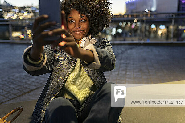 Smiling young woman taking selfie with smart phone at night