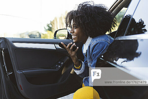 Cheerful woman talking on mobile phone through speaker sitting in car