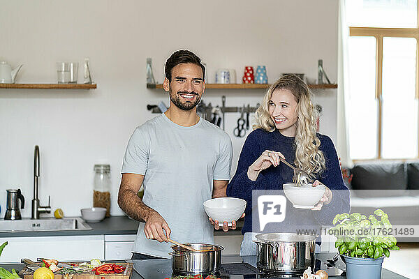 Happy young man and woman holding bowls standing in kitchen at home
