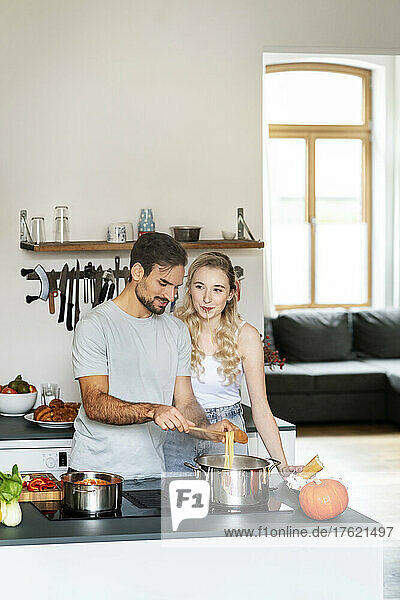 Blond woman talking with boyfriend making pasta in kitchen at home