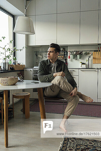 Nachdenklicher junger Mann sitzt am Tisch in der Küche
