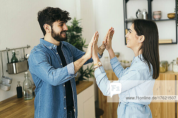 Smiling couple giving high-five to each other in kitchen at home