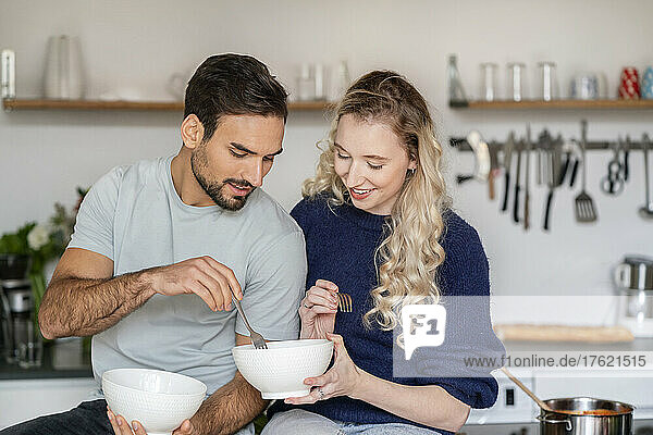 Smiling young woman sharing food with boyfriend in kitchen at home