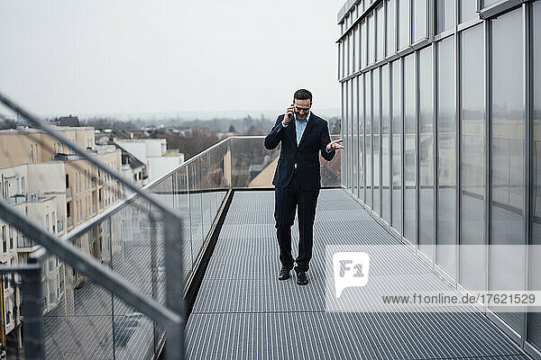 Happy businessman talking on mobile phone walking on balcony