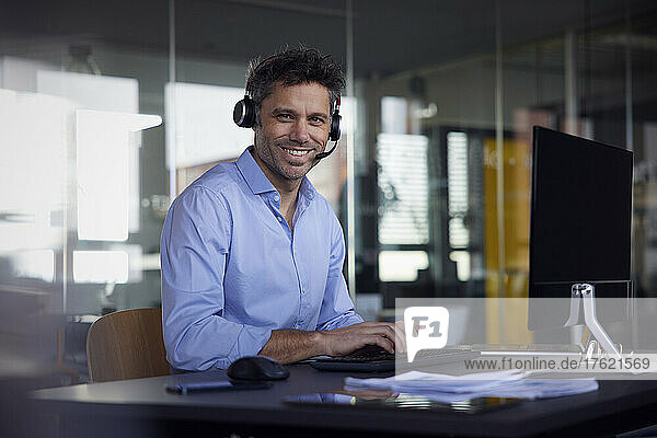 Happy businessman wearing wireless headset sitting at desk in office