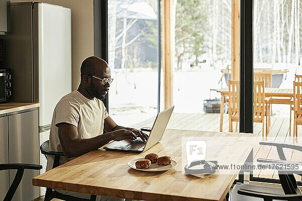 Young man using laptop at table in kitchen at home