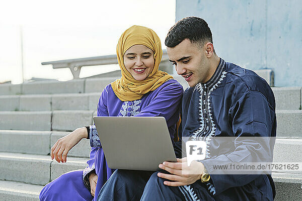 Young man using laptop sitting with woman on staircase