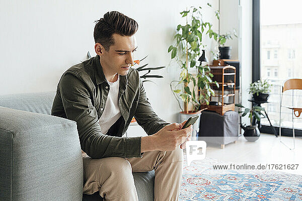 Young man text messaging through smart phone in living room at home