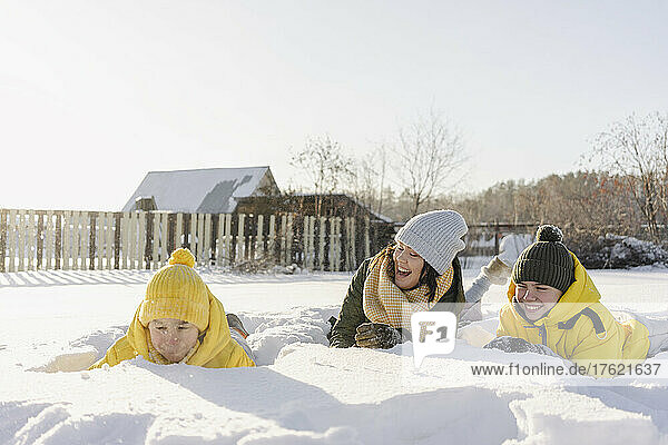 Playful boys with mother lying on snow in winter