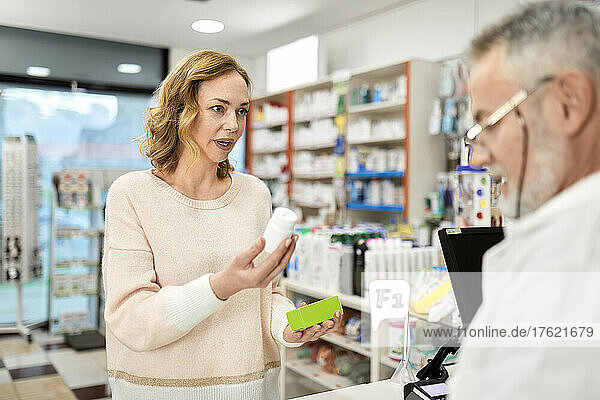 Customer holding bottle of medicine talking with pharmacist at checkout counter